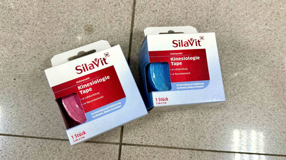 Kinesiologie-Tape im Test: Zwei Packungen des Kinesiologie-Tape in unterschiedlichen Farben auf einem Fließenboden.