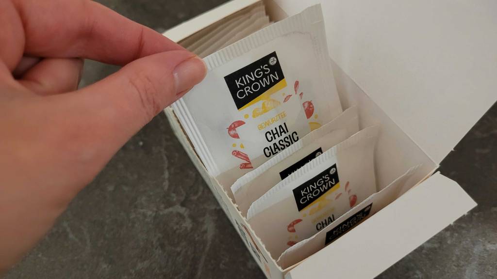 Getestet: Chai-Tee in der Packung, aus der eine Hand einen weißen Beutel mit Tee nimmt.