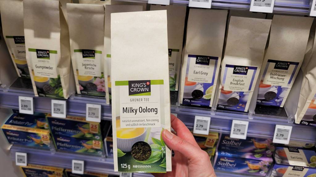 Eine Hand hält einen 125-g-Beutel mit Milky-Oolong-Tee im Test vor einem Drogeriemarktregal.