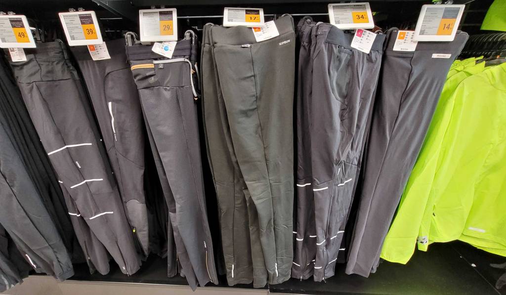 Eine graue Thermo-Laufhose für Herren im Test hängt zusammen mit weiteren langen Hosen an einem Verkaufsstand.
