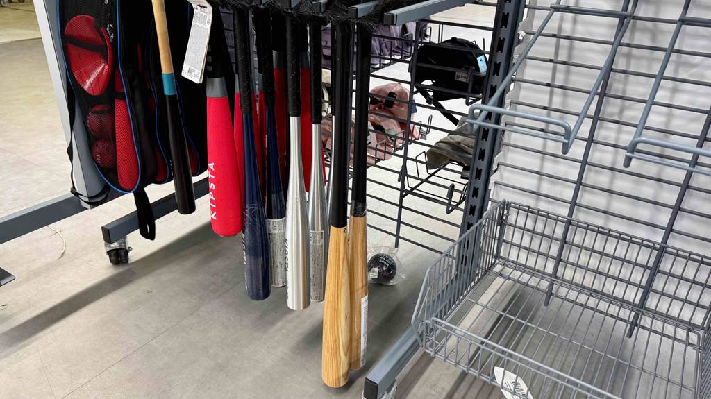 Aluminium-, Holz und Kunststoff-Baseballschläger im Test befinden sich hängend an einem Verkaufsregal.