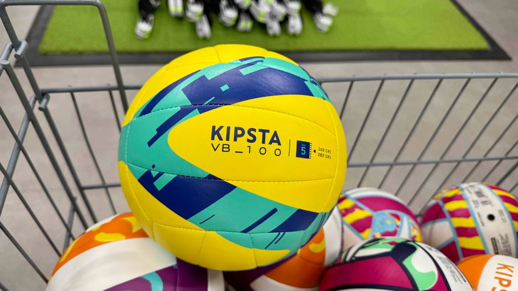 In einem Korb auf mehreren Bällen befindet sich der türkis-gelbe, getestete Volleyball VB_100 von KIPSTA.