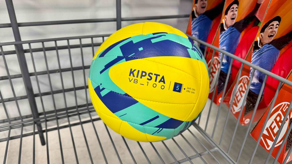 Der türkis-gelbe, getestete Volleyball VB_100 von KIPSTA liegt in einem Verkaufskorb im Geschäft.