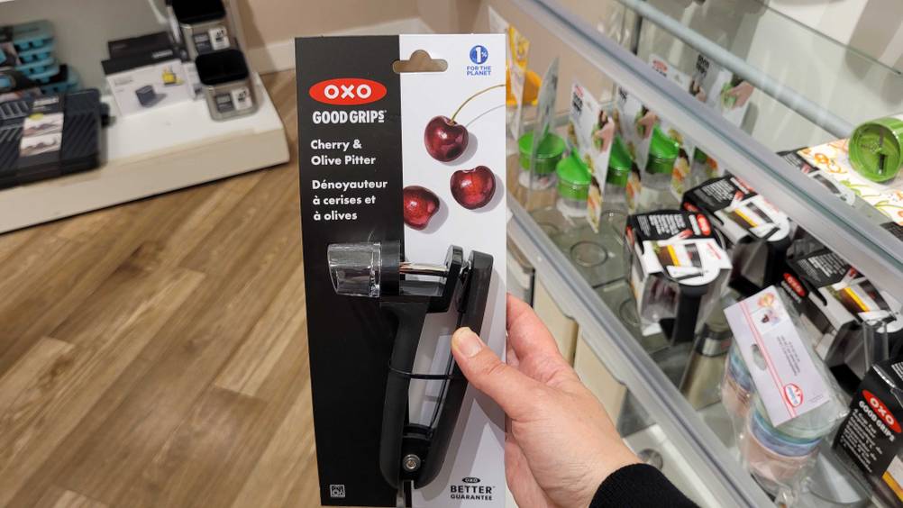 Getestet: Eine Hand hält einen originalverpackten Kirschentkerner, im Hintergrund Regale mit anderen Produkten.
