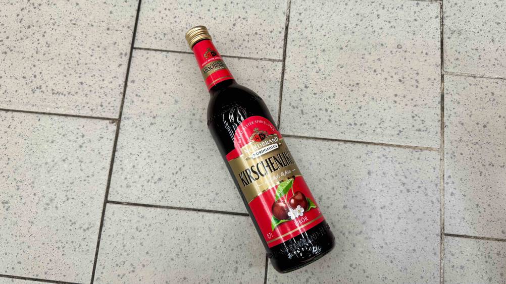 Eine Flasche Kirschlikör im Test liegt auf einem Fließenboden.