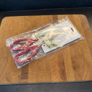 Die Kitchenaid-Allzweck-Küchenschere liegt komplett in Plastik verpackt auf einer Holzplatte