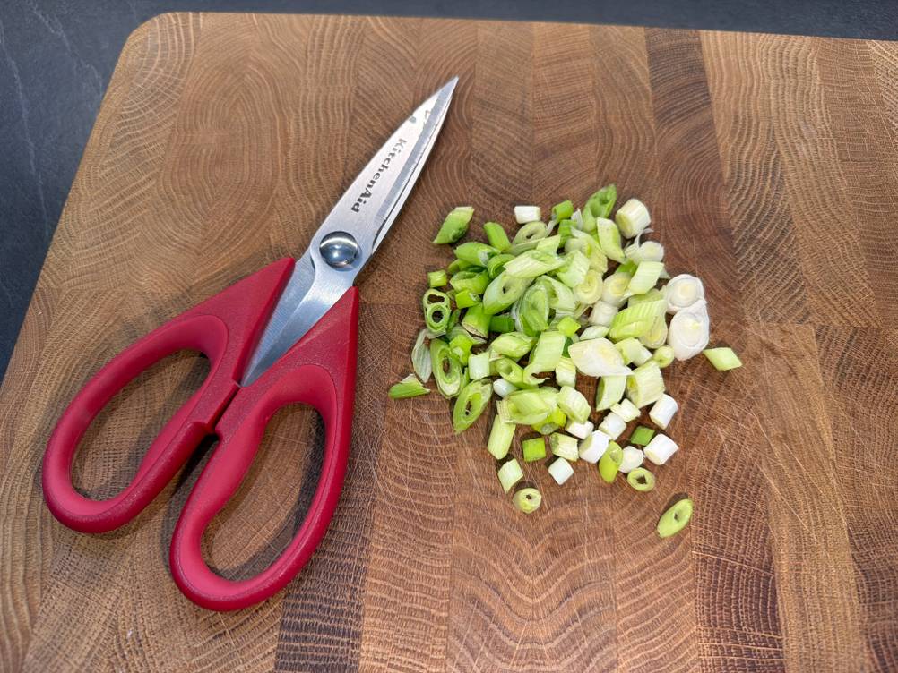 Die Kitchenaid-Allzweck-Küchenschere liegt neben einem Haufen Frühlingszwiebeln