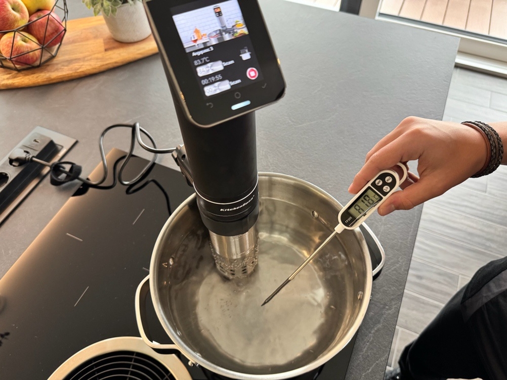 Eine Hand hält einen Temperaturfühler, der 81,8 °C anzeigt, in einen Kochtopf mit Wasser
