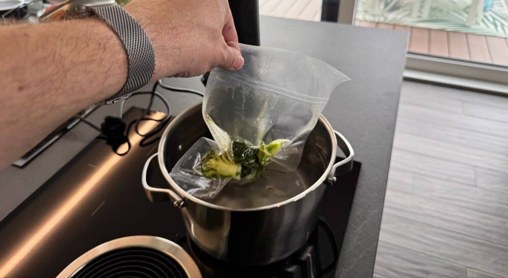 Eine Hand hält vakuumierten Brokkoli in einen Kochtopf mit Wasser
