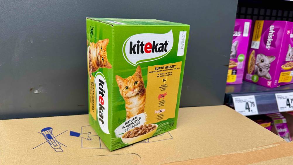 Eine Packung Kitekat-Katzenfutter im Test vor einer grauen Wand auf einem Karton stehend.