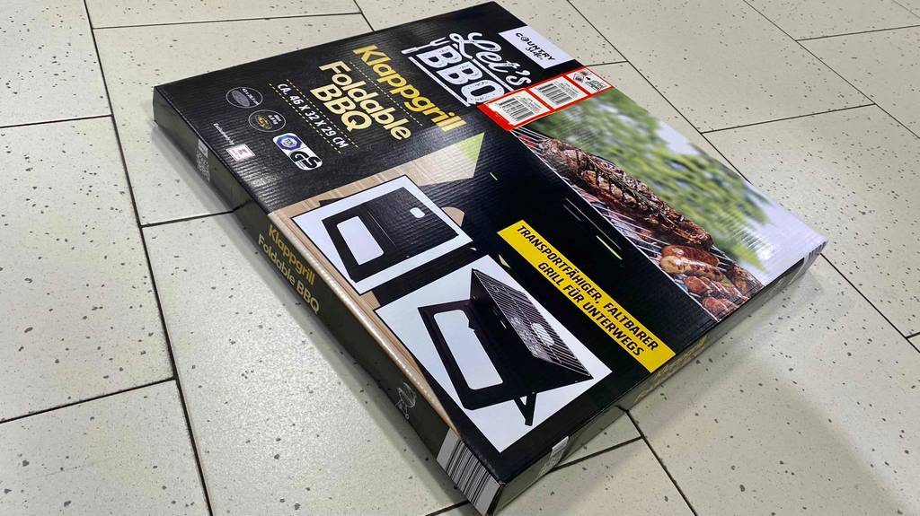 Getesteter Klappgrill befindet sich verpackt auf dem Boden. 