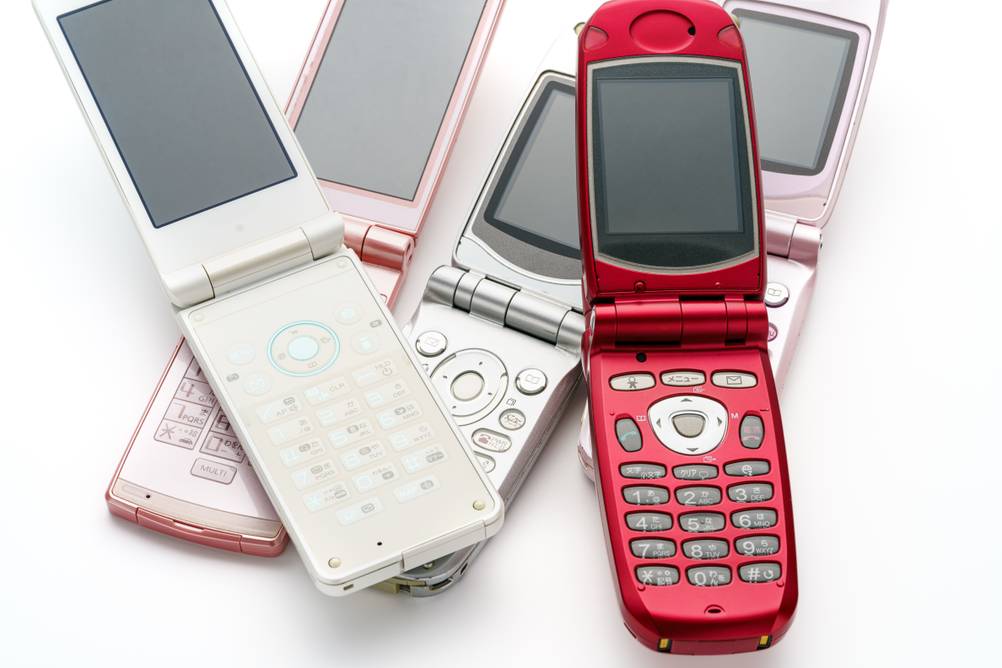 Klapphandys in verschiedenen Farben, rot, silber und rosa, liegen auf einer Oberfläche nebeneinander.