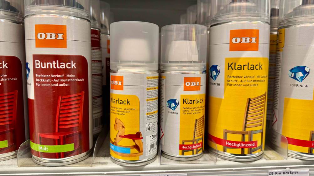 Mehrer Dosen des getesteten Klarlacks in unterschiedlichen Größen in einem Verkaufsregal neben anderen Produkten.