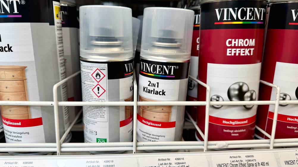 Mehrere Dosen des Klarlack-Spray im Test in einem Verkaufsregal neben anderen Produkten.
