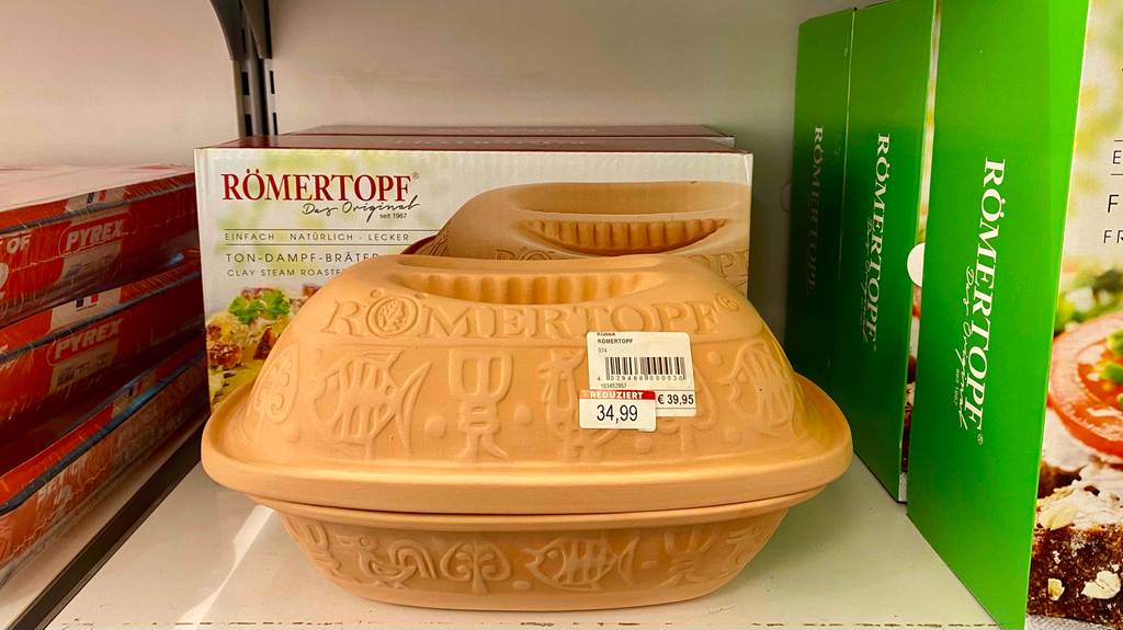 Römertopf-Test: Vorderansicht auf einen geschlossenen Ton-Römertopf inklusive Preisetikett zwischen anderen Bratbehältern auf einem Verkaufsregal.
