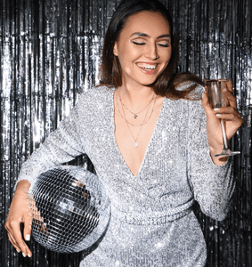 Klebe-Bh-Test: Eine Frau in einem silber-glitzernden Kleid hält eine Discokugel und ein Glas Sekt in der Hand. 