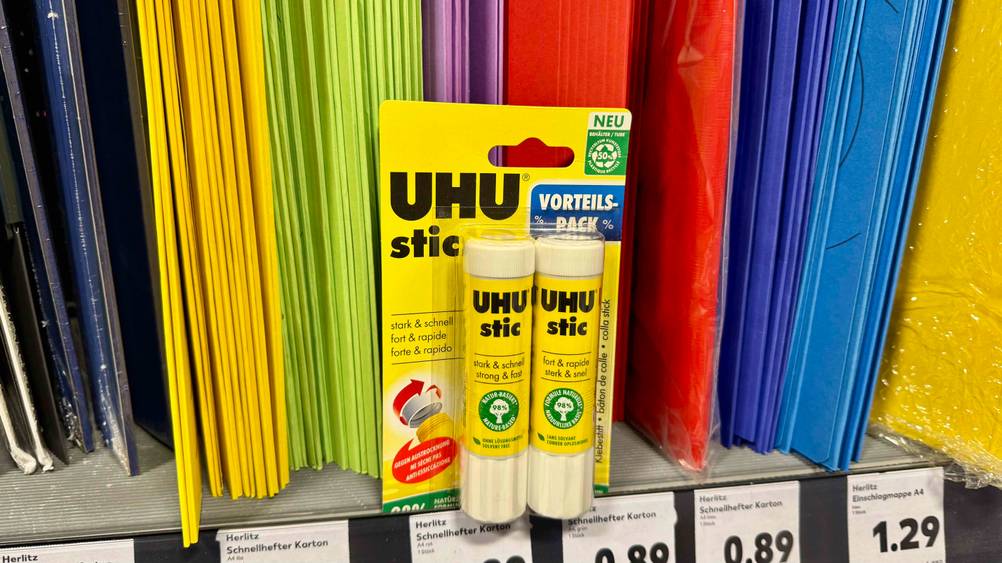 Klebestift getestet: Transparent verpackte Stifte stehen vor bunten Hüllen in einem. Regal.