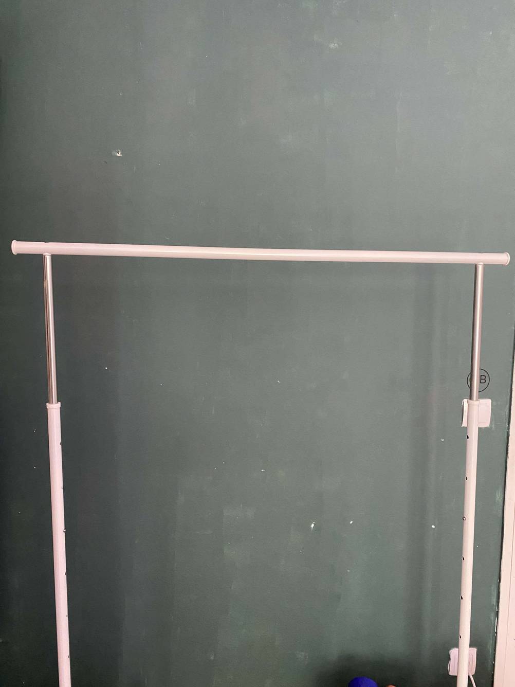 Die Kleiderständer-Stange eines getesteten Kleiderständers vor einer grauen Wand.