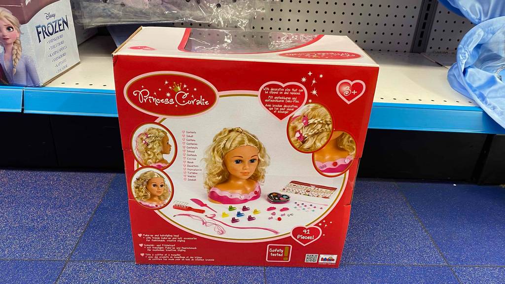 Schminkpuppe im Test: ein Puppenkopf Princess Coralie befindet sich in seiner Originalverpackung inklusive Schminkutensilien in einem Verkaufsbereich.