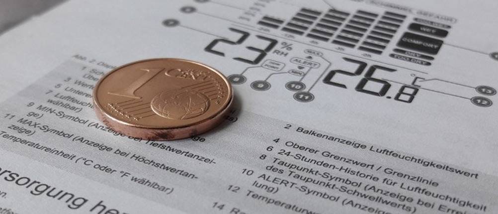 Nahaufnahme Bedienungsanleitung eines Hygrometers mit einer Cent-Münze darauf liegend.