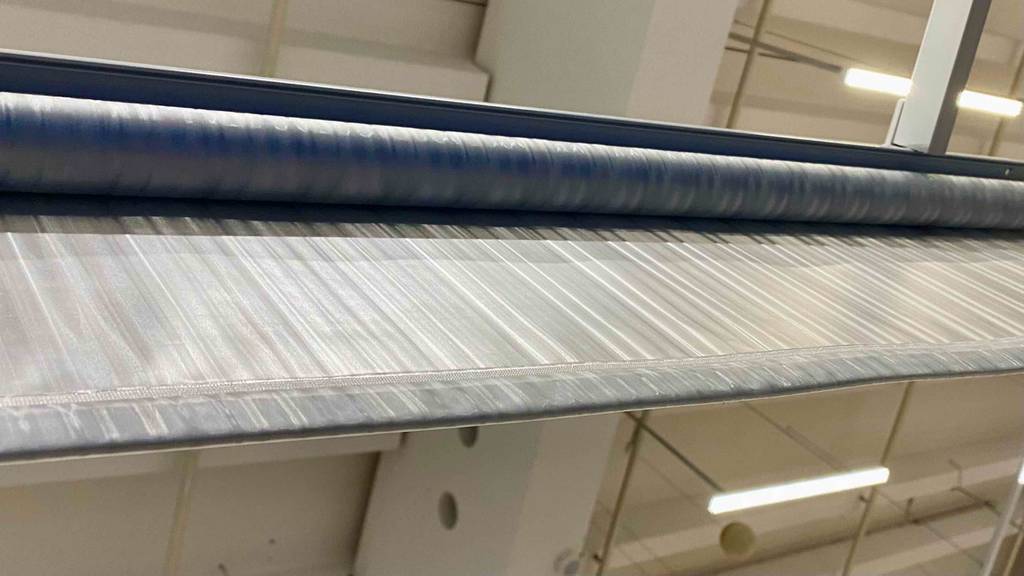 Detailansicht von unten eines aufgerollten, grau, transparenten Duschrollos im Test.