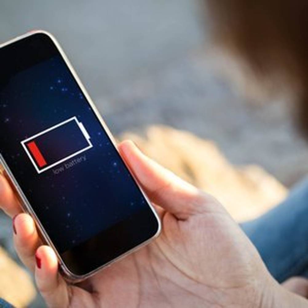 Frau, die auf ihr Smartphone schaut, dessen Akku leer ist