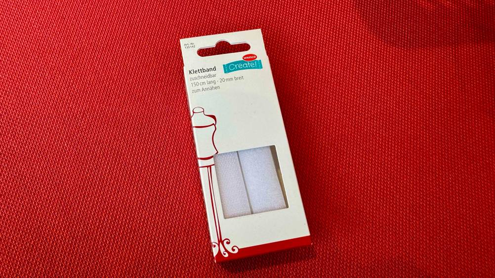 Auf einem roten Polster liegt das Klettband im Test in der Originalverpackung.