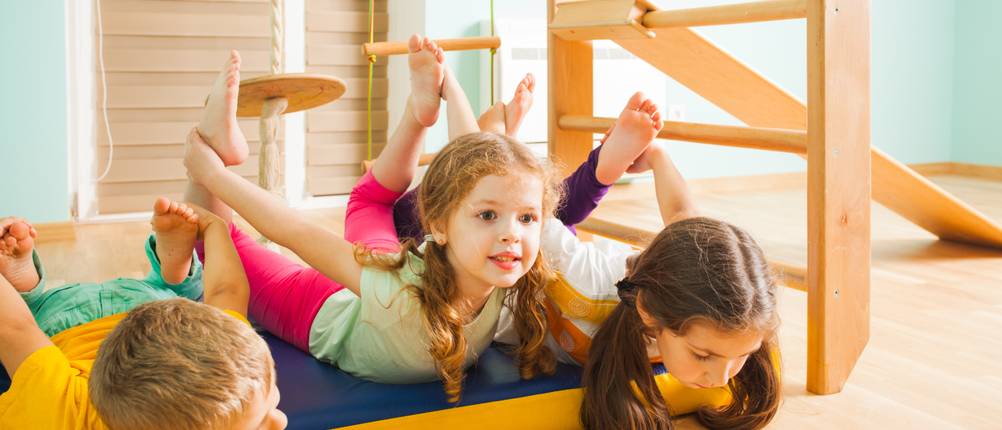Klettergerüst Indoor im Test: Zwei Mädchen und ein Junge spielen in einem Zimmer an einem Klettergerüst aus Holz.