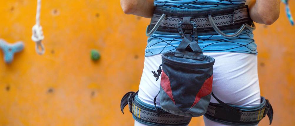 Klettergurt-Erwachsene-Test: Eine Frau mit einem Klettergurt und einer Chalkbag steht vor einer Kletterwand. 