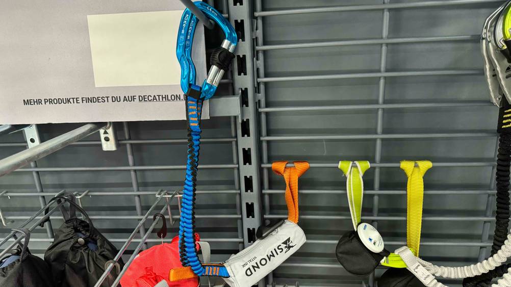 Ein getestetes Klettersteigset an einer Regalwand mit Karabinern und Schlaufen befestigt.