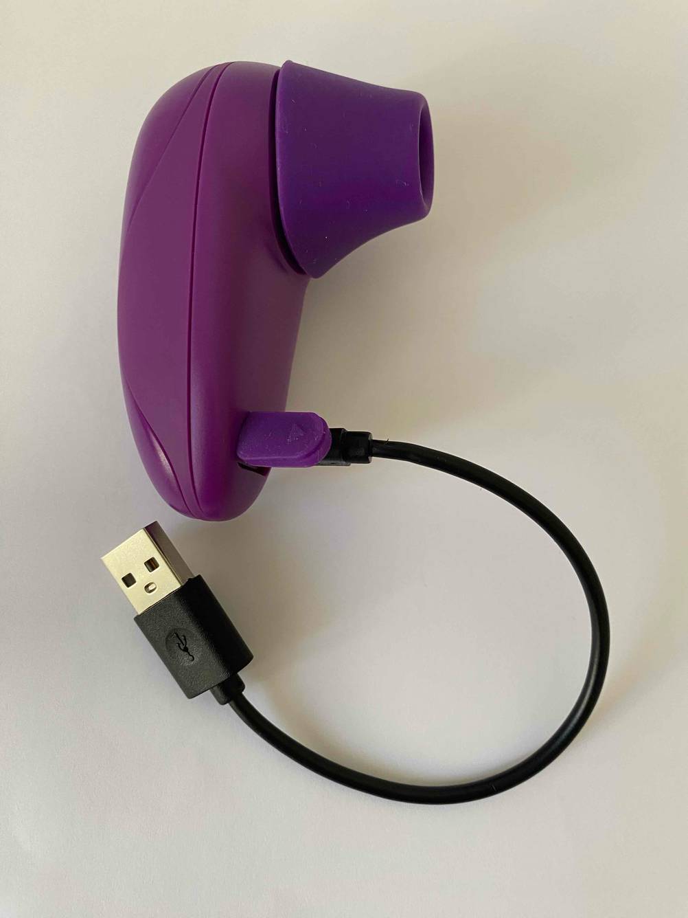 Der getestete Klitorissauger mit USB-Ladekabel auf einer hellen Fläche.