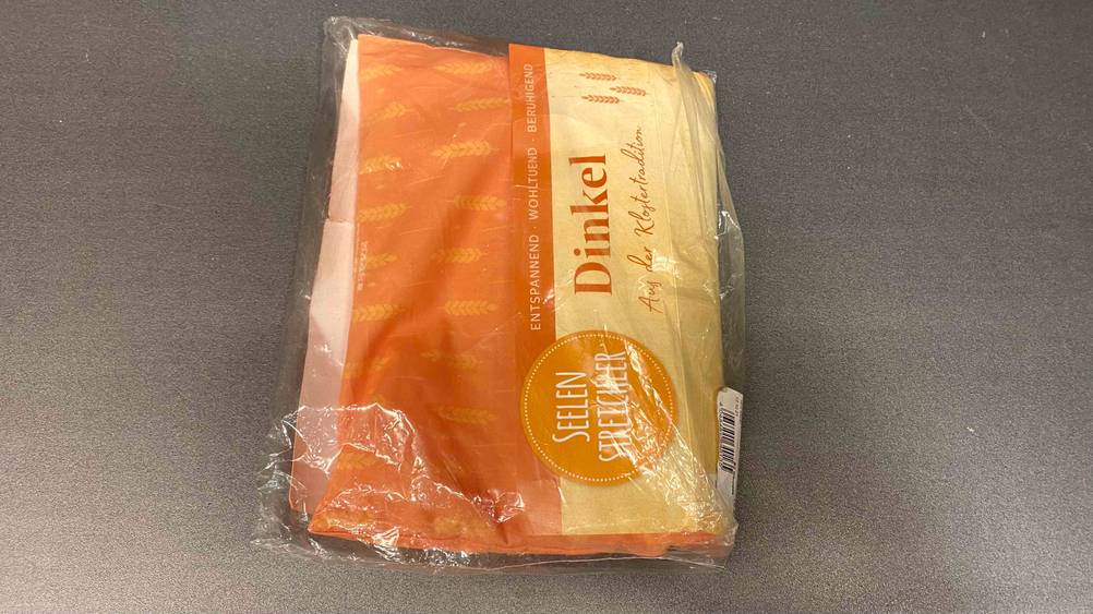 Ein getestetes Dinkelkissen in seiner Verpackung auf einer grauen Fläche.