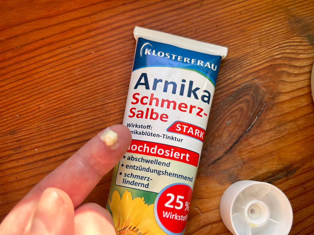 Getestet: Auf einem Finger, der über einer Tube Arnika-Salbe ist, ist etwas Salbe.