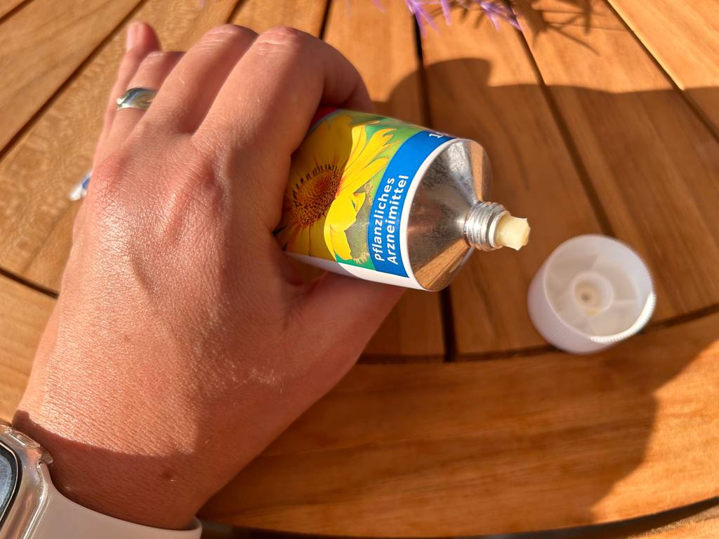 Eine Hand drückt etwas aus einer geöffneten Tube mit Arnika-Salbe, um sie zu testen.