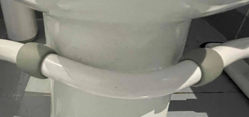 Nahaufnahme der Befestigung am unteren Teil der Toilette von einer grau-weißen WC-Aufstehhilfe im Test.