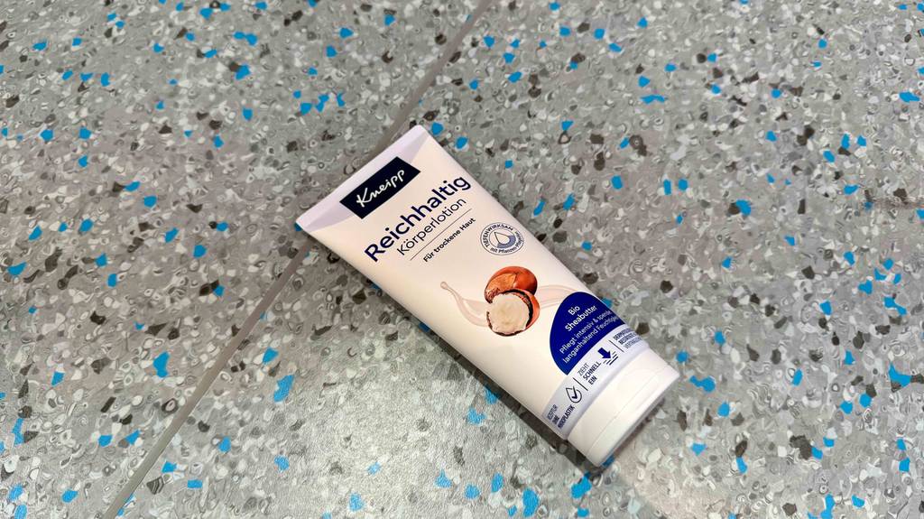Eine Tube getestete Körperlotion für trockene Haut liegt auf einem gesprenkelten Boden.