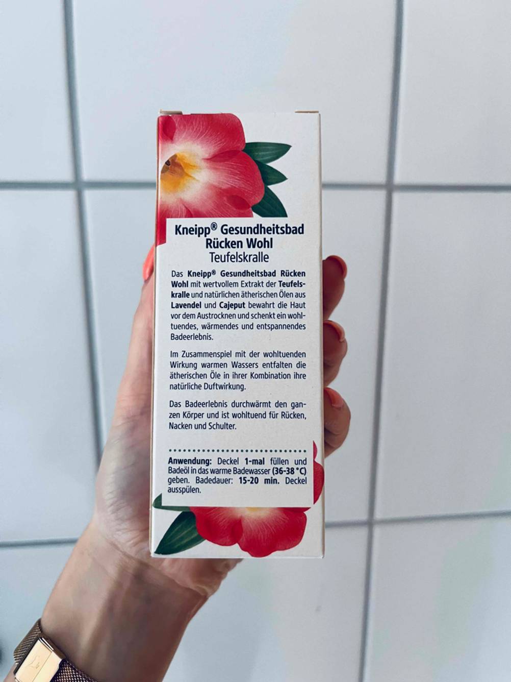 Teufelskralle-Test: Hand hält Originalverpackung Gesundheitsbad Rückenwohl von Kneipp, mit Fokus auf die Produktbeschreibung, vor weißer Fliesenwand.