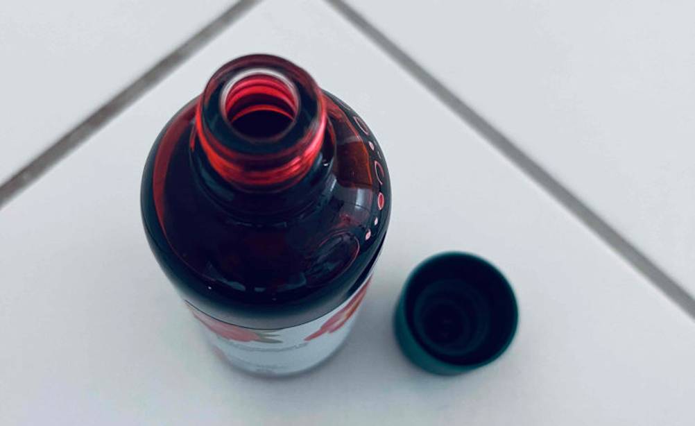 Teufelskralle getestet: Aufnahme von oben auf eine blickdichte geöffnete Flasche neben grünem Verschluss auf weißen Fliesen.