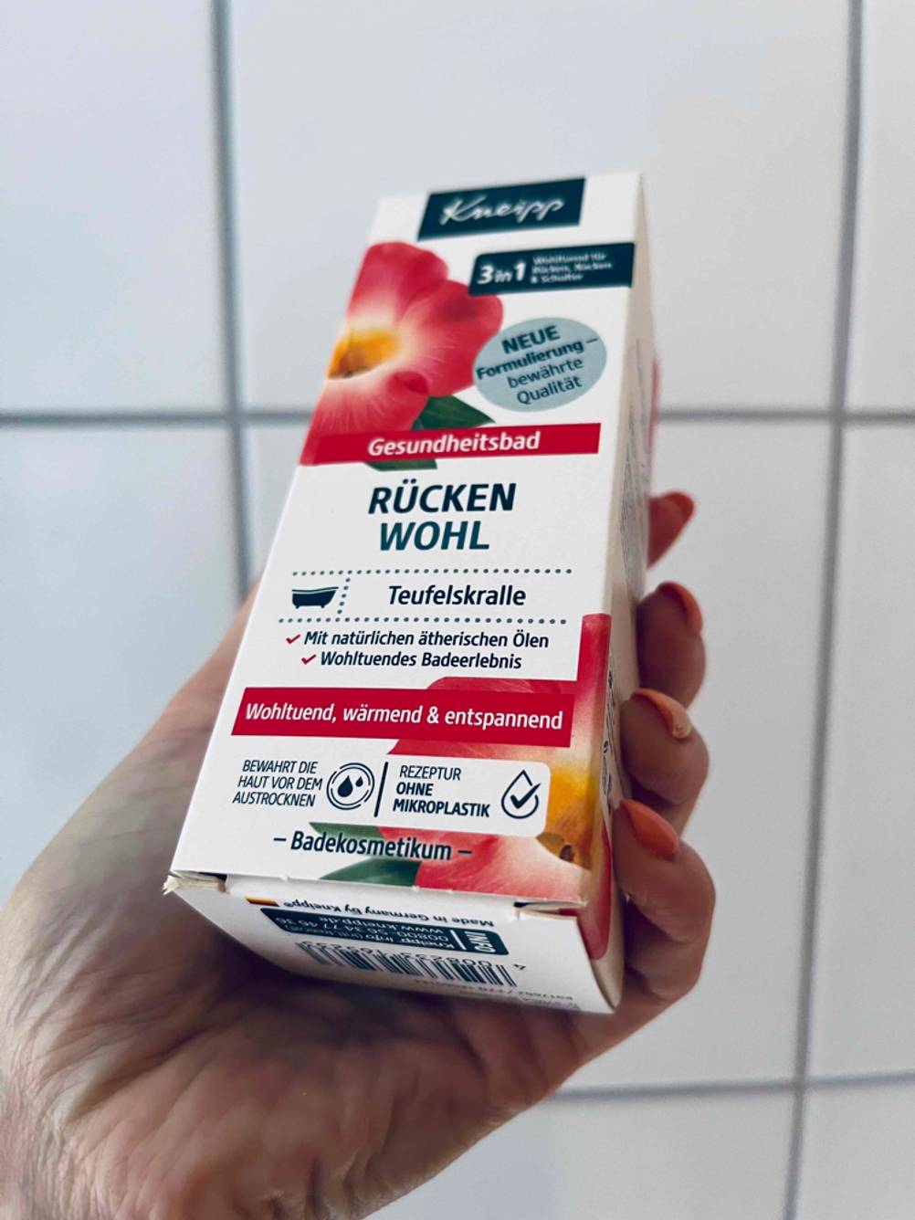 Teufelskralle im Test: Hand hält eine Originalverpackung Gesundheitsbad Rückenwohl von Kneipp vor weißen Fliesen.
