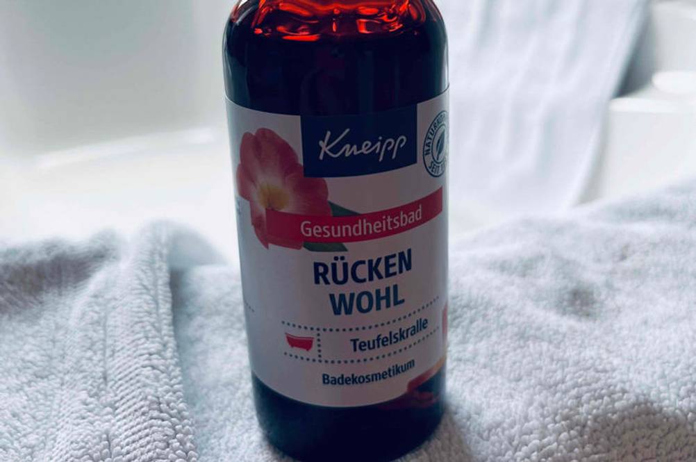 Eine Flasche getestete Teufelskralle von Kneipp steht auf einem Handtuch vor einer Badewanne.
