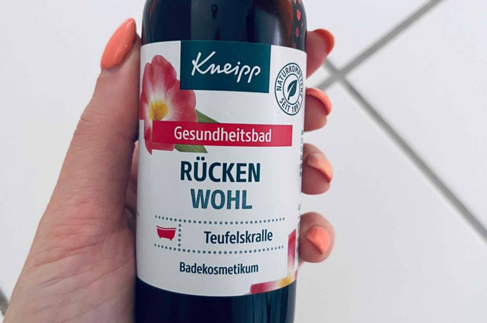 Hand hält eine Flasche getestete Kneipp Teufelskralle vor weißen Fliesen.