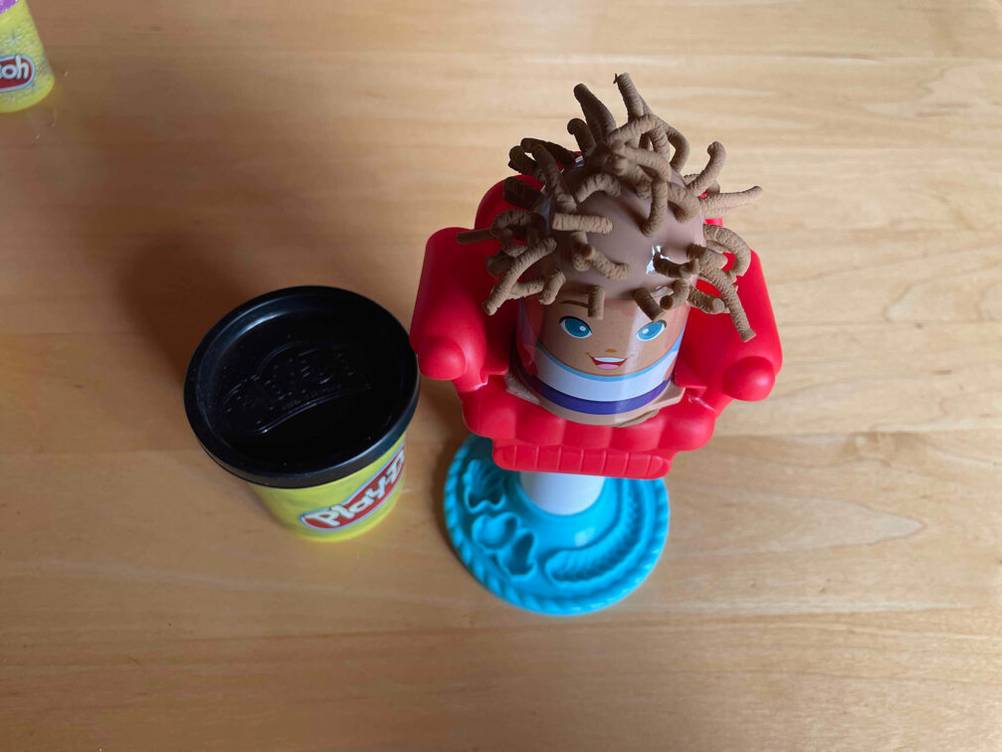 Neben einer Figur steht eine Dose der getesteten Knete auf einer Holzfläche.