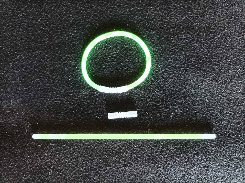 Zwei getestete Knicklichter auf einer dunklen Fläche, eines zu einem Armband geschlossen.