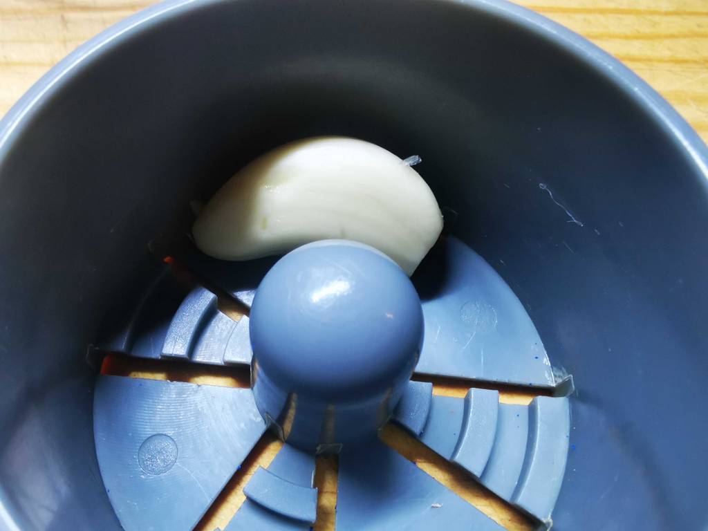 Eine Knoblauchzehe liegt im Schneider eines Knoblauchschneiders im Test.