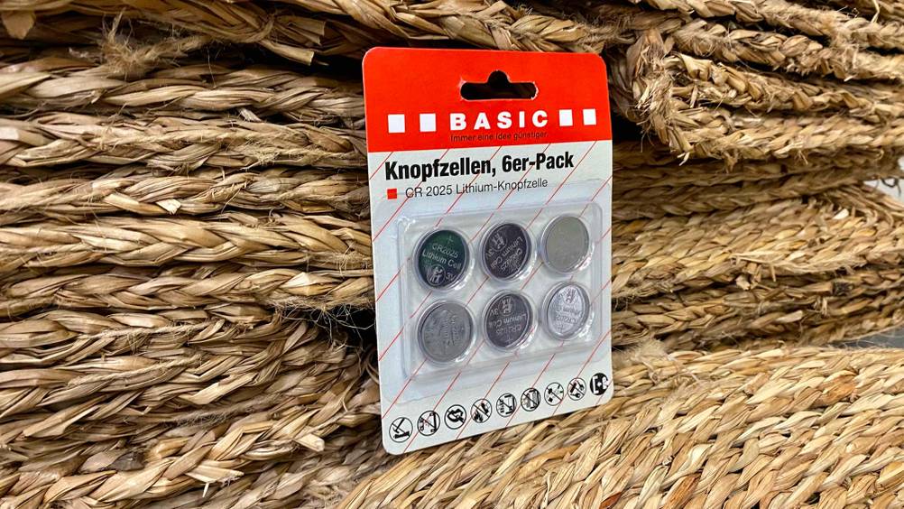 Eine Packung der getesteten Knopfzellen lehnt an Korbmatten.