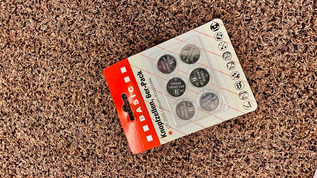 Auf dem Boden befindet sich ein getestetes 6-er-Pack Knopfzellen.
