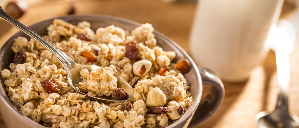 eine Schüssel Knuper-Müsli mit Löffel und einem Glas Milch