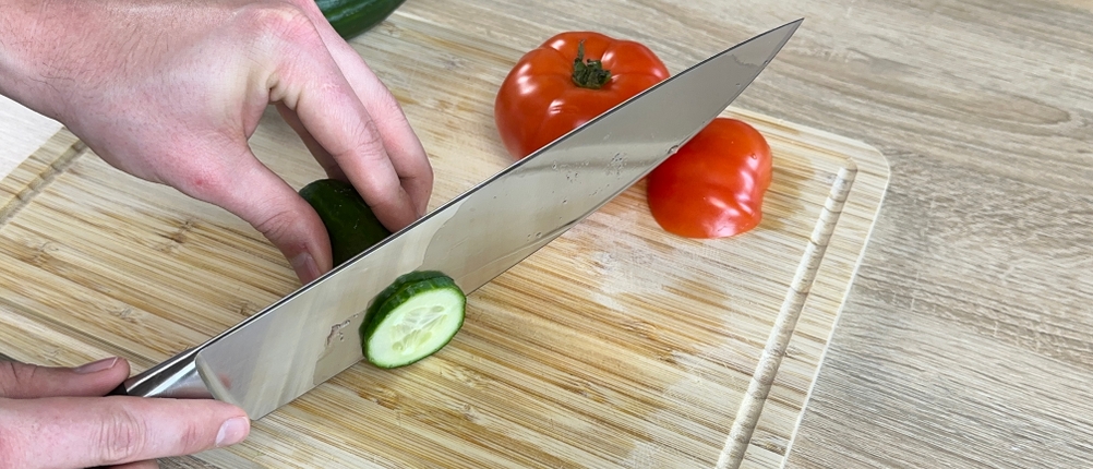 Das F.-Dick-1905-Messer schneidet eine Gurke auf einem Holzbrett. Eine Tomate liegt daneben.