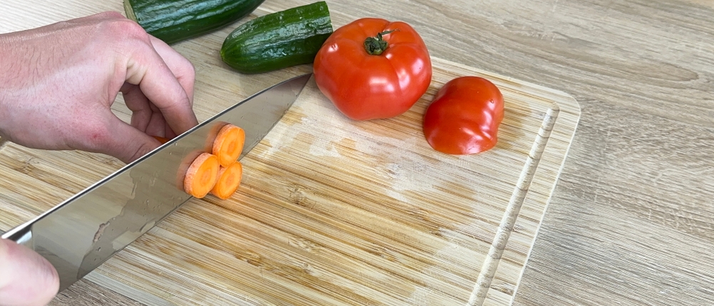 Das F.-Dick-1905-Kochmesser wird zum Schneiden einer Karotte verwendet. Auf dem Brett liegt weiteres Gemüse bereit.