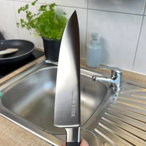 Das gereinigte F.-Dick-1905-Kochmesser wird über dem Spülbecken gehalten. Die Klinge ist glänzend und sauber.